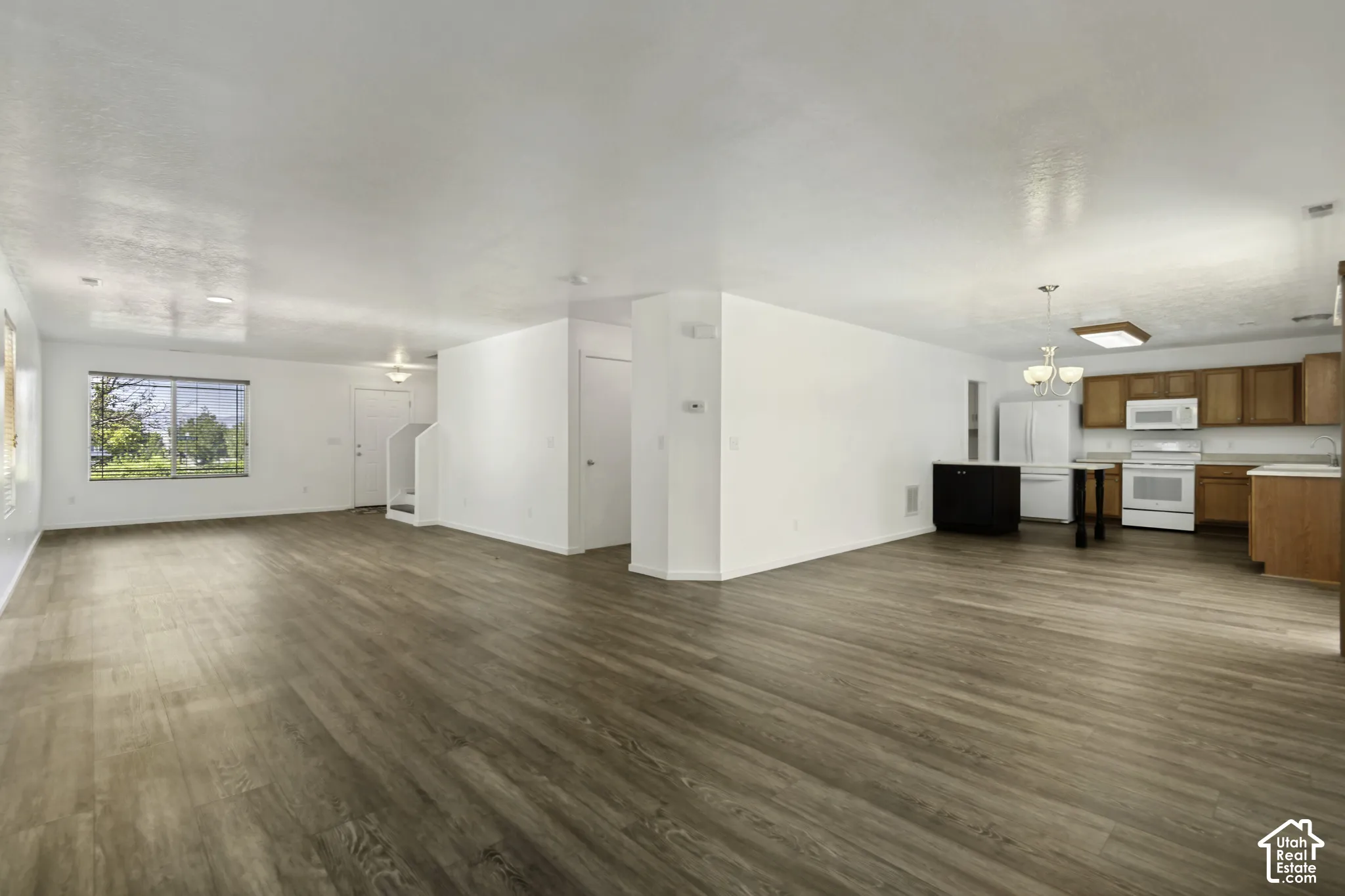 Expansive open-concept living area featuring wood-finish flooring and a kitchen with wood cabinetry, white appliances, and a central island