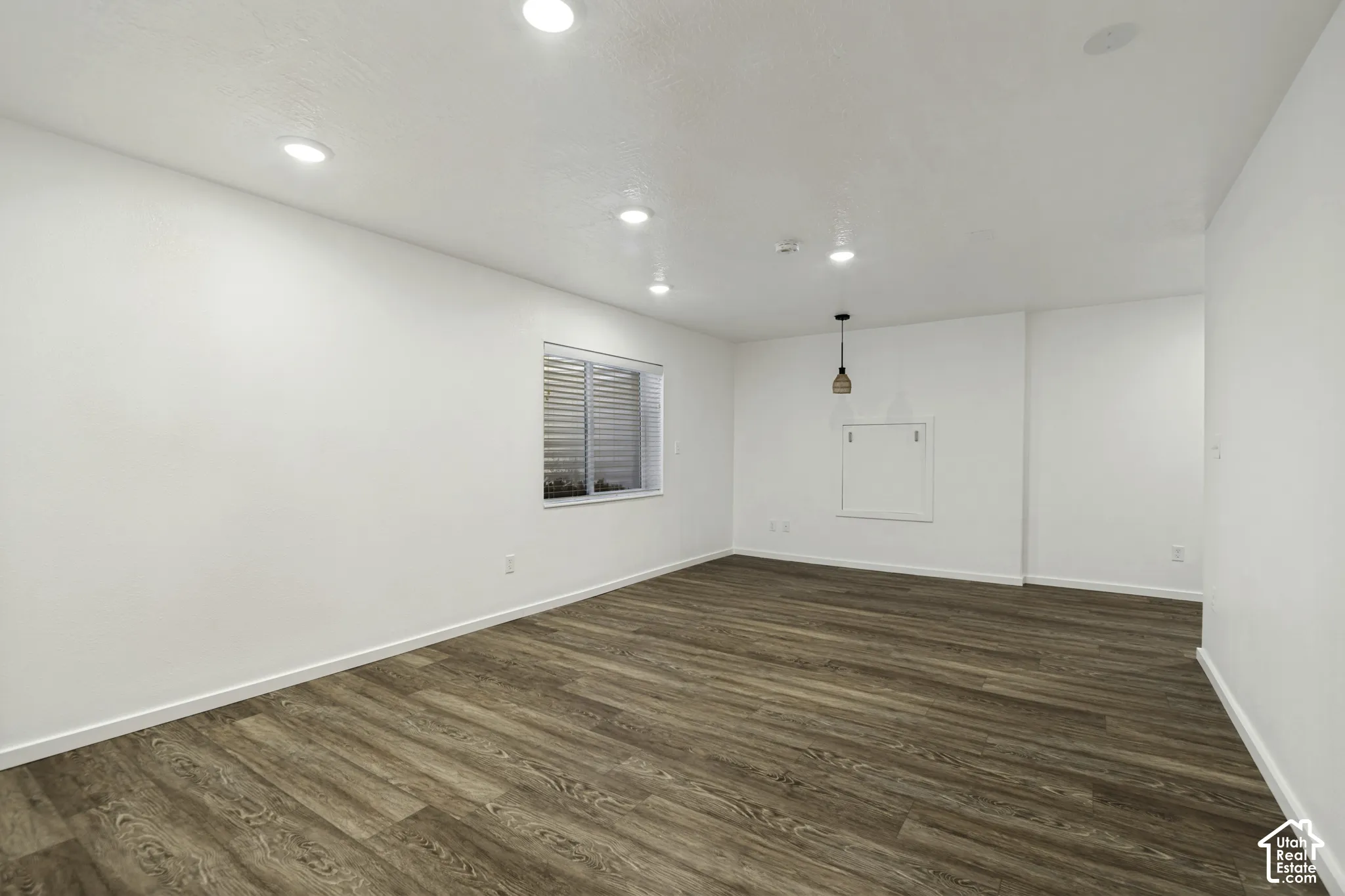 Spacious room featuring wood-finish flooring, recessed lighting, and a pendant light fixture