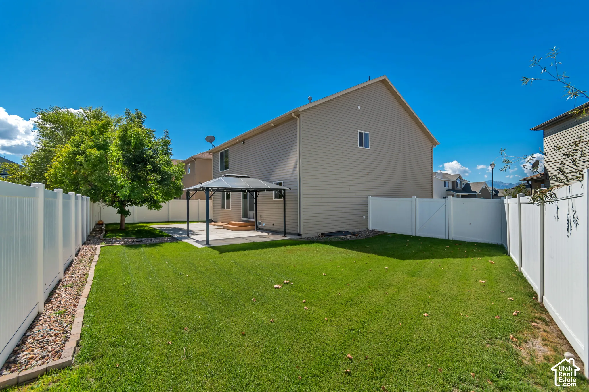 Expansive backyard featuring a green lawn, full privacy fencing, a paved patio, and a gazebo