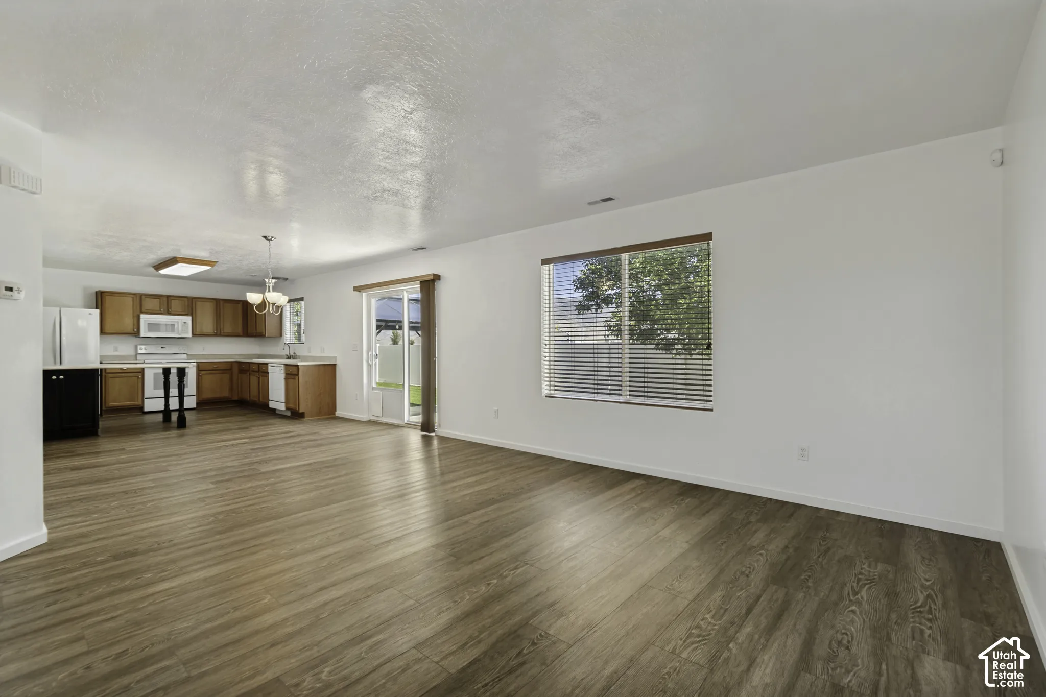 Spacious room with wood-finish flooring, white walls, and a large window with blinds