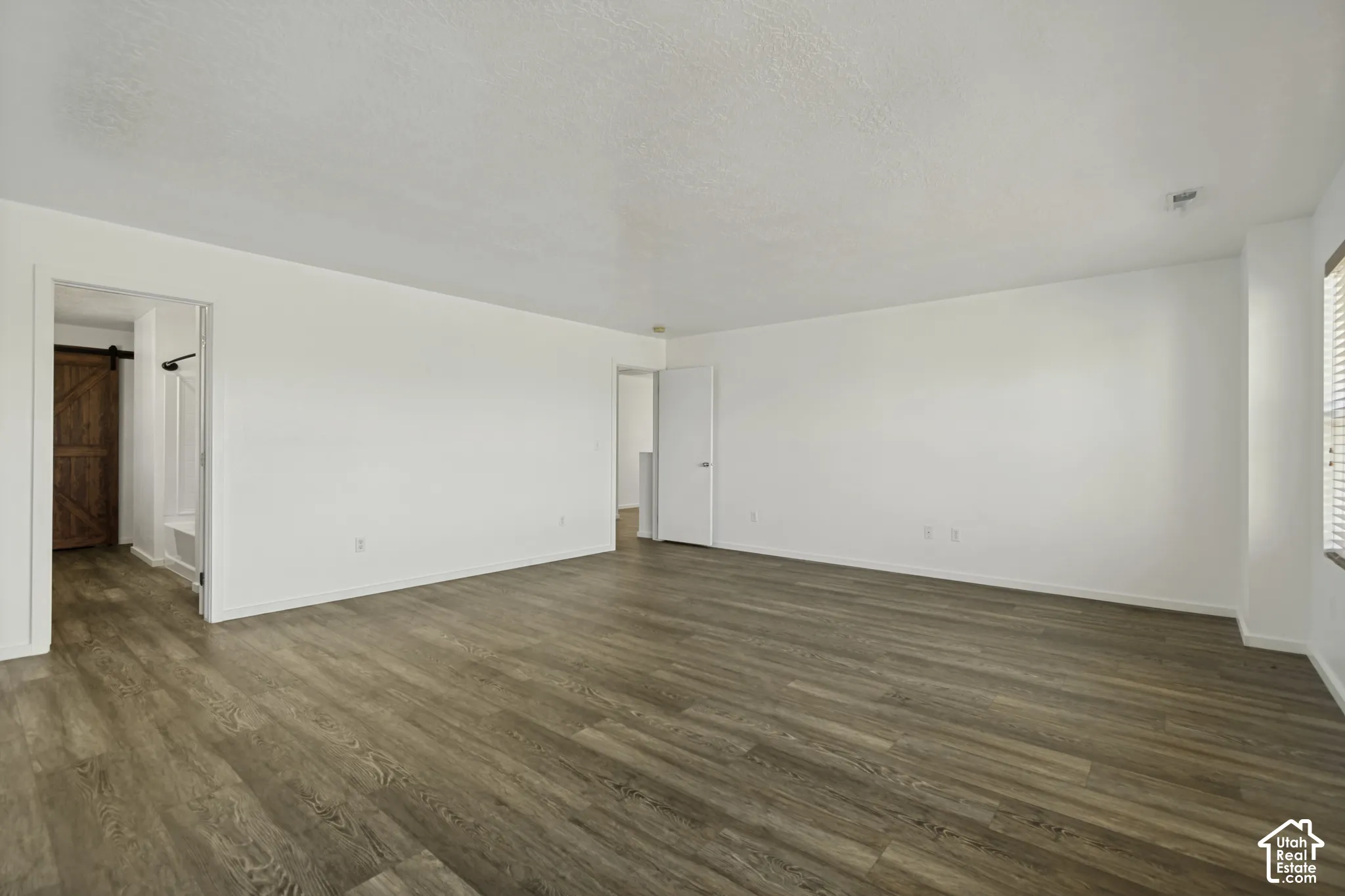 Expansive room featuring wood-finish flooring, white walls, and a window with blinds