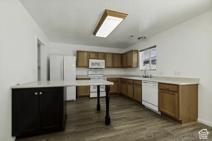 Kitchen featuring wood-finish flooring, light wood cabinetry, light countertops, white appliances, and a breakfast bar with dark wood base