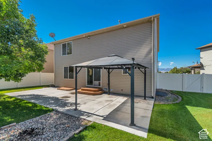 Expansive concrete patio with a covered gazebo structure, manicured lawn, and a white privacy fence