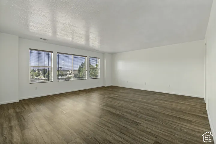 Expansive room with wood-finish flooring, white walls, and multiple windows with blinds