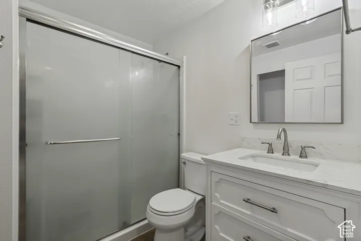 White vanity with drawer storage, rectangular undermount sink, brushed nickel faucet, framed mirror, and a shower with frosted sliding glass doors