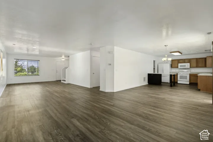 Expansive open-concept living area featuring wood-finish flooring and a kitchen with wood cabinetry, white appliances, and a central island