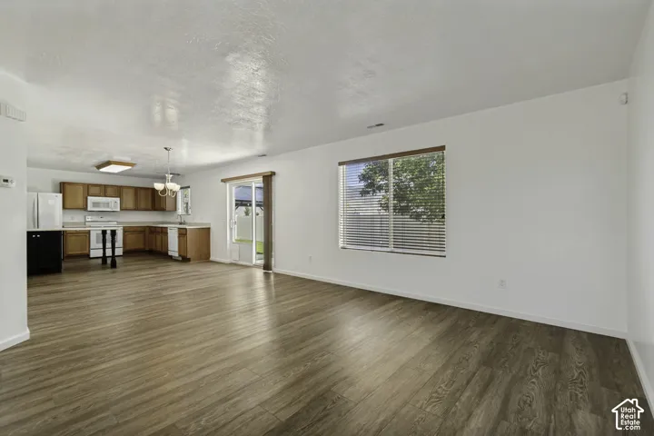 Spacious room with wood-finish flooring, white walls, and a large window with blinds