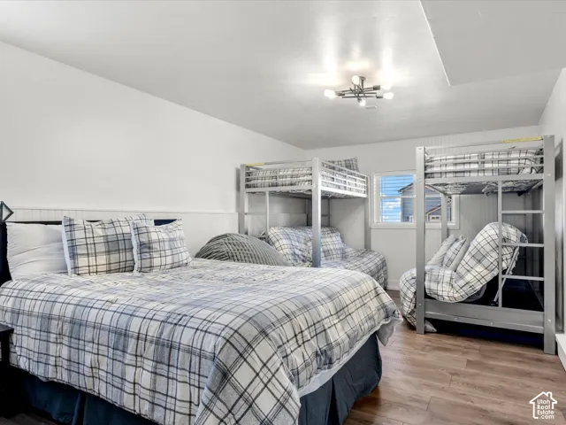 Basement bunk room.  Recessed ceiling panel, wood-finish flooring, white paneling, multiple bunk beds, and a window with natural light