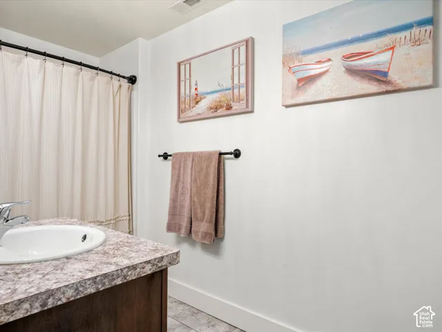 Basement bathroom.  White walls with tile flooring, a dark wood-finish vanity, and a shower with a curved rod