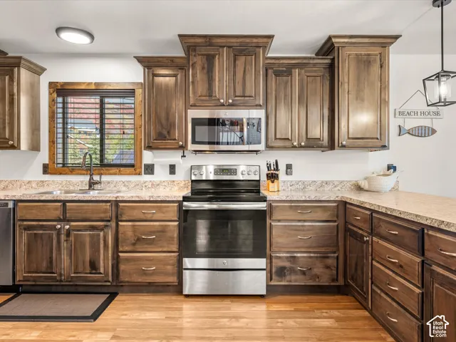 Kitchen featuring wood-finish cabinetry, stainless steel appliances, laminate countertops, a stainless steel sink, and wood-finish flooring