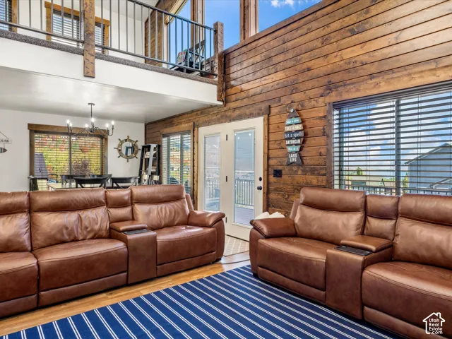 Wood paneling accent wall, balcony with metal railing, double glass-paneled exterior door, large windows with blinds, and wood-finish flooring