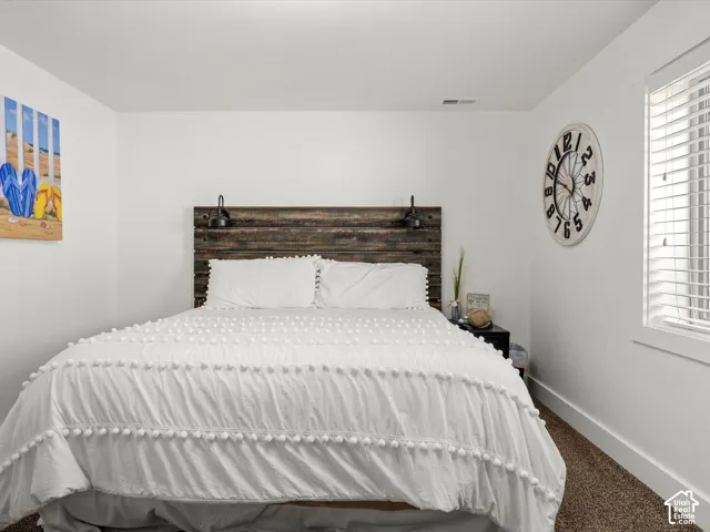 Basement bedroom. Distressed wood-finish headboard with integrated sconce lighting, white walls, and a window with blinds