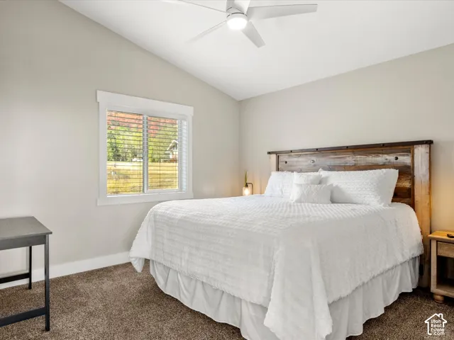 2nd floor bedroom. Vaulted ceiling with a contemporary ceiling fan, dual-pane window with white blinds, and carpeted flooring