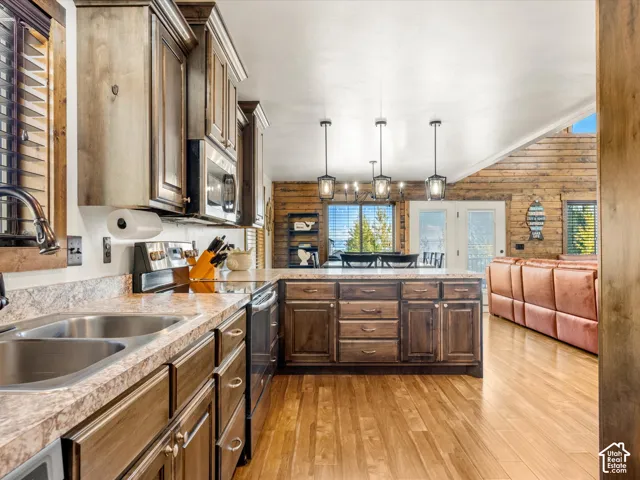 Kitchen featuring wood-finish cabinetry, stainless steel appliances, a double basin sink, and a central island with pendant lighting