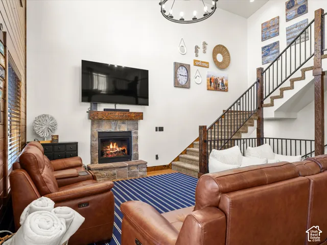 Stone fireplace with a wood mantel, carpeted staircase with wood newel posts and metal balusters, and a contemporary chandelier