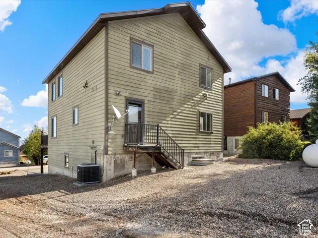 Two-story exterior with horizontal siding, multiple windows, a rear entry with steps, and a gravel lot
