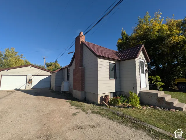 Metal roof, brick chimney, concrete steps, two-car garage, and stucco siding
