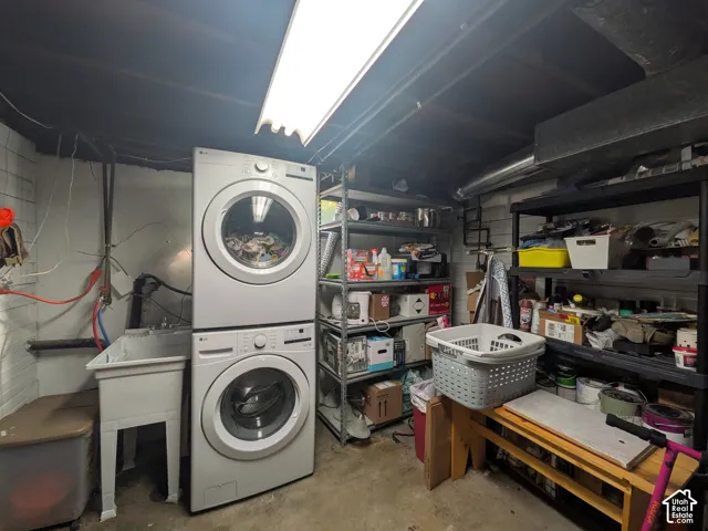 Utility space featuring a stacked washer and dryer, laundry sink, and overhead fluorescent lighting
