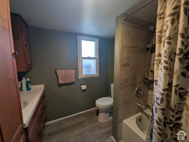 Bathroom featuring a wood-finish vanity with a white countertop and integrated sink, a built-in wood-finish cabinet, a window, a white toilet, and a tiled shower with a tub