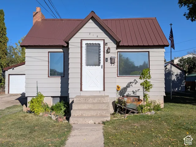 Light-colored siding exterior with a brown metal roof, featuring a detached garage and a brick chimney