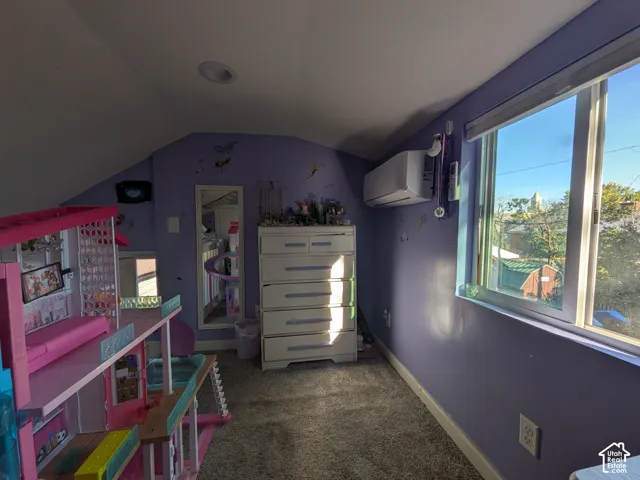 Sloped ceiling room featuring a window, built-in recessed lighting, and wall-mounted climate control unit