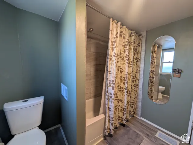 Bathtub with tiled surround, wood-finish flooring, and a wall-mounted mirror