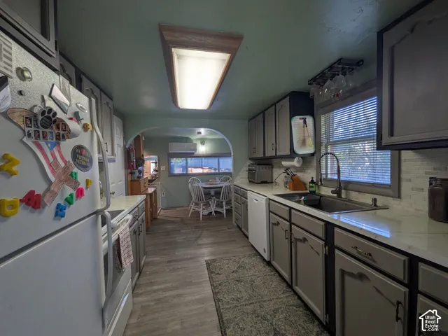Wood-finish flooring, white countertops, tile backsplash, built-in cabinetry, and a kitchen sink with a gooseneck faucet