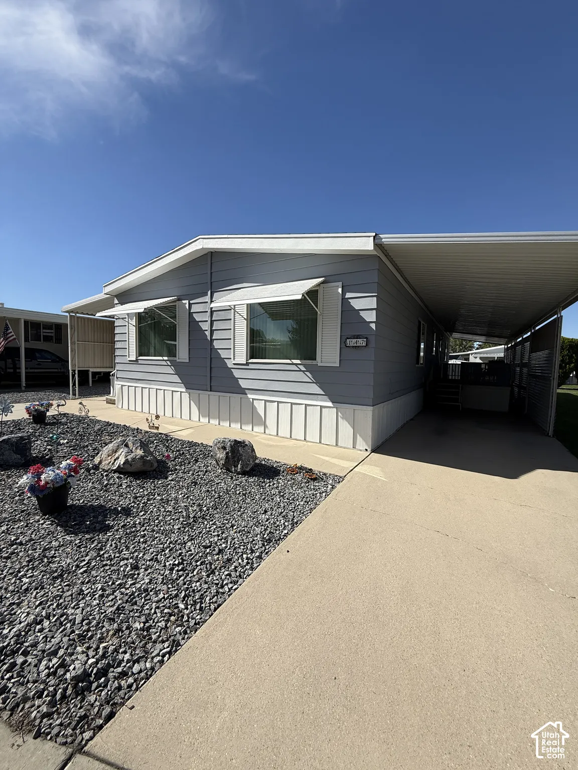 Light blue siding with white trim, two windows featuring awnings, a concrete driveway, and a rock-landscaped front yard
