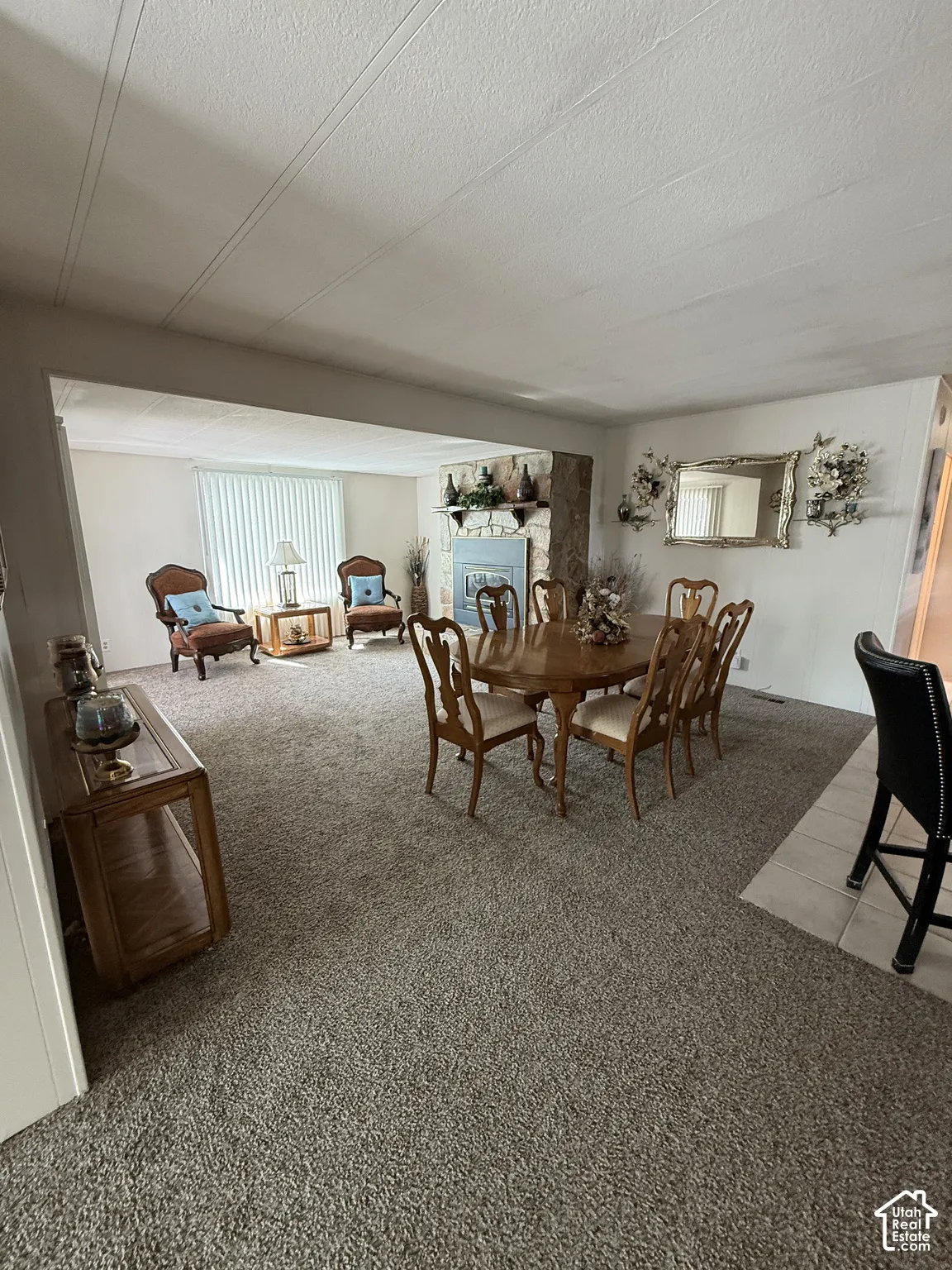 Open-concept living space featuring a natural stone fireplace, neutral carpeting, and a built-in shelf