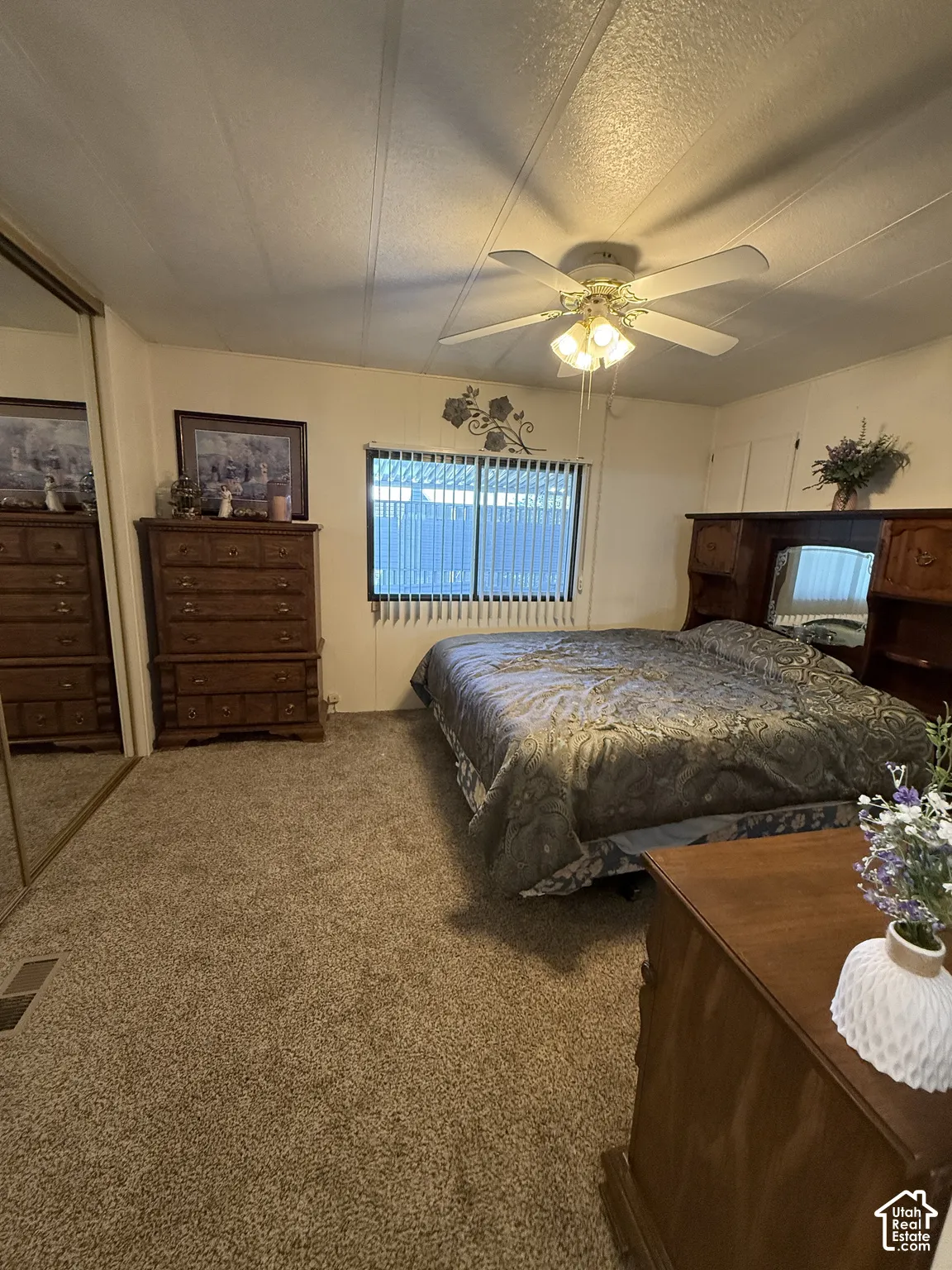 Textured carpeting, window with horizontal blinds, ceiling fan with integrated lighting, and mirrored closet doors