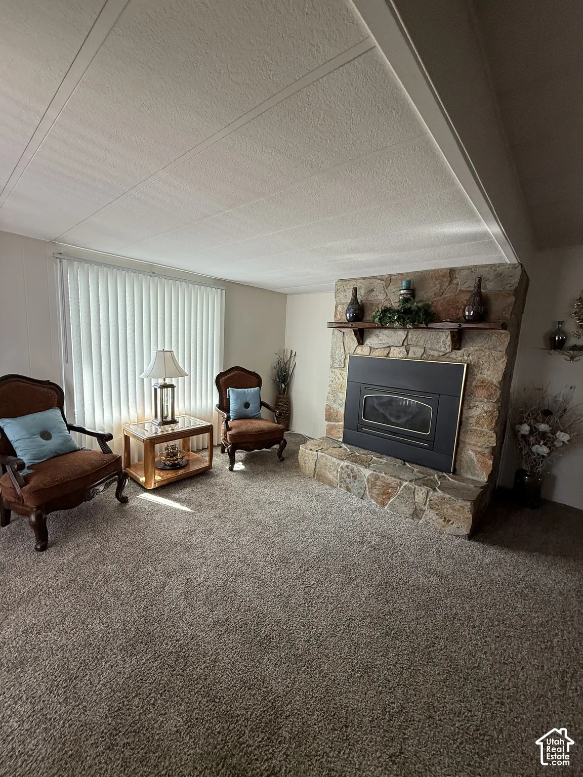 Stone-clad fireplace with hearth, wall-to-wall carpeting, and vertical window blinds