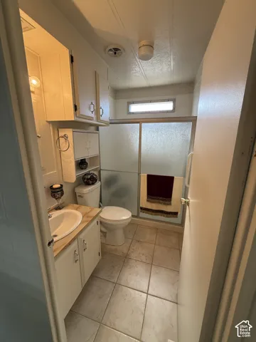 Bathroom featuring a vanity with an integrated sink, built-in cabinetry, ceramic tile flooring, and a shower with a frosted glass enclosure