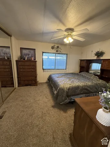 Textured carpeting, window with horizontal blinds, ceiling fan with integrated lighting, and mirrored closet doors