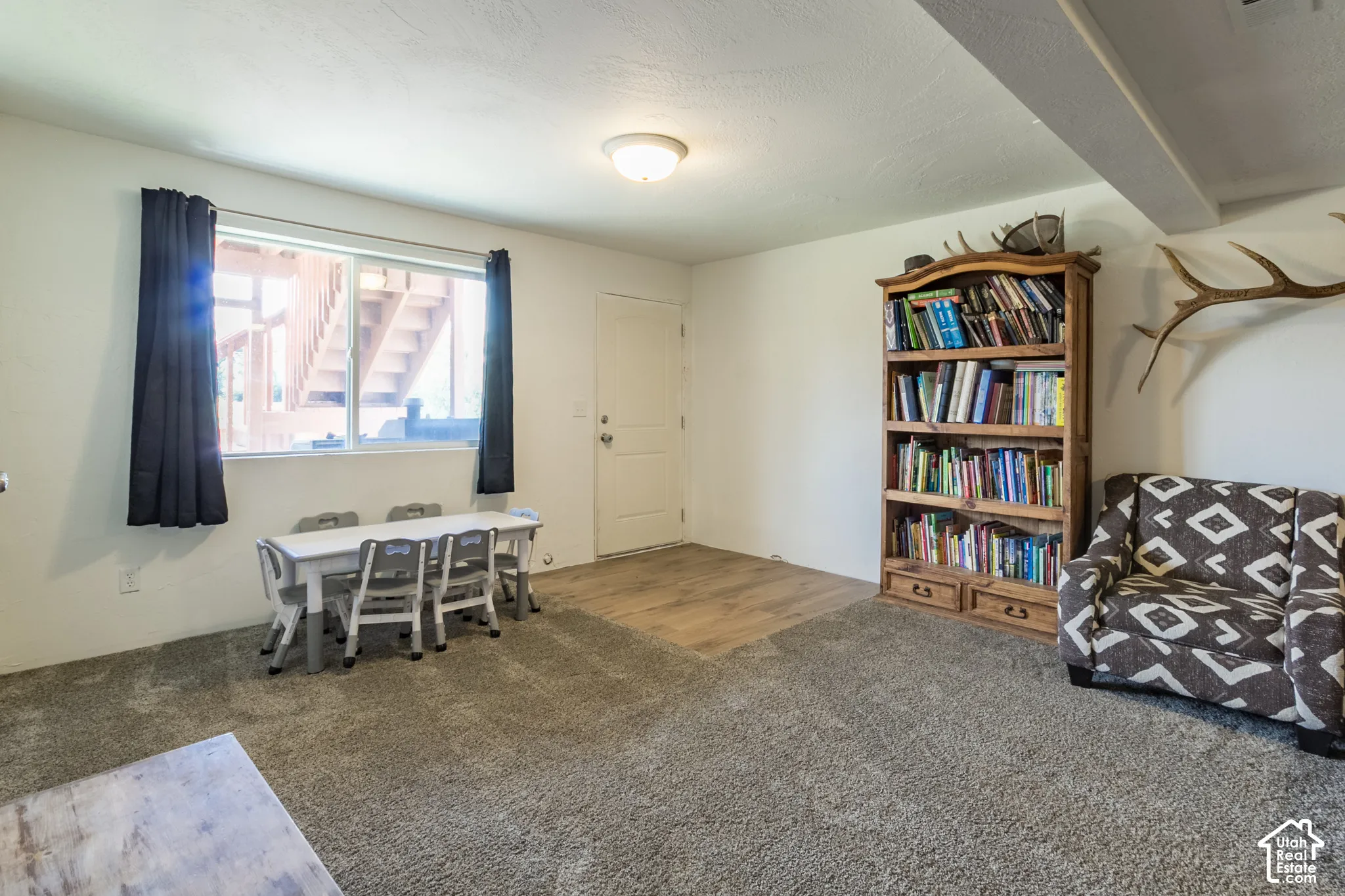 Carpeted flooring, wood-finish flooring, built-in shelving, white walls, and a window with black curtains