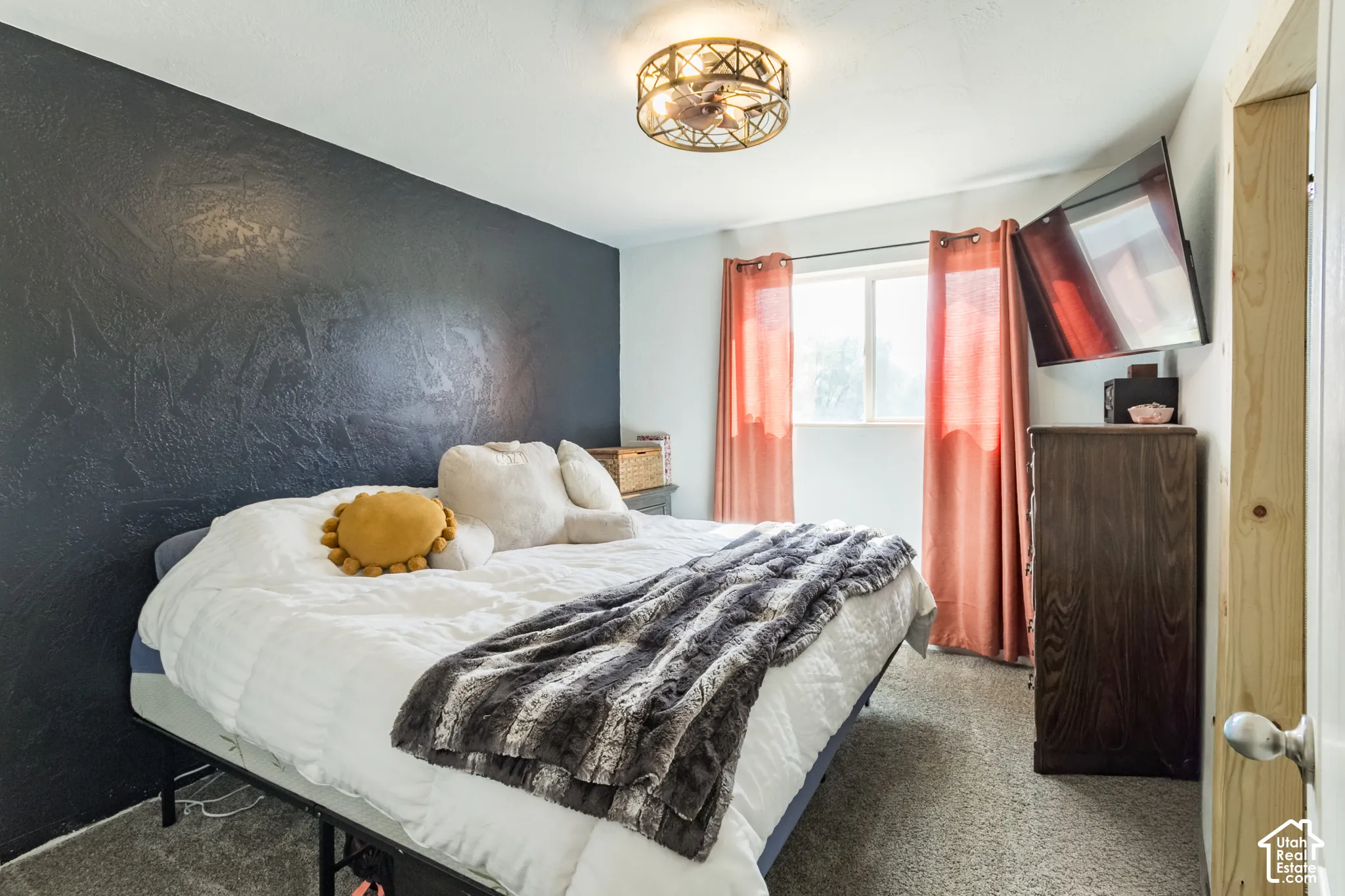 Textured accent wall, window with natural light, ceiling-mounted light fixture, wood-finish dresser, and carpet flooring