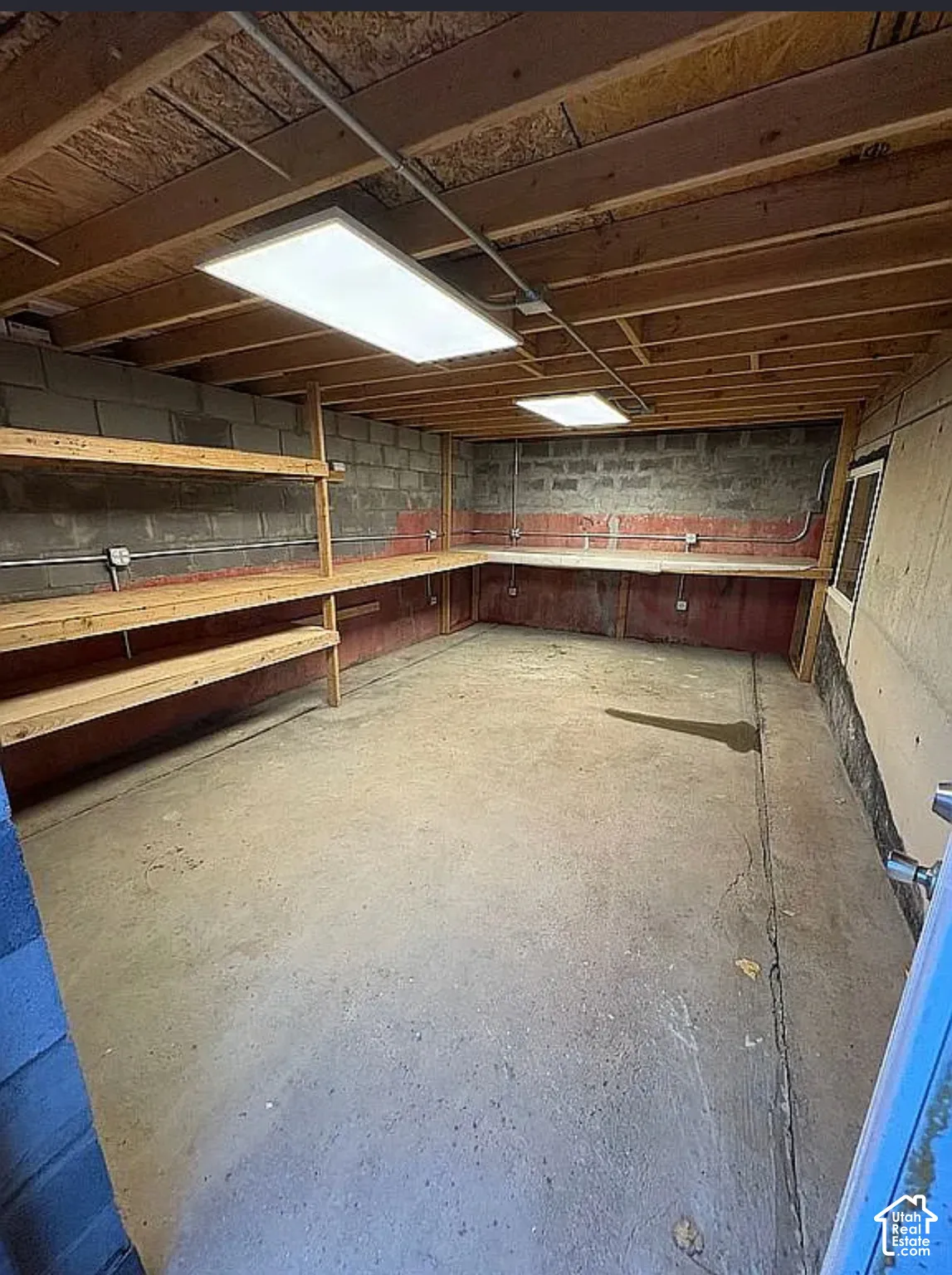 Concrete flooring, exposed joist ceiling, built-in shelving, built-in workbench, overhead lighting