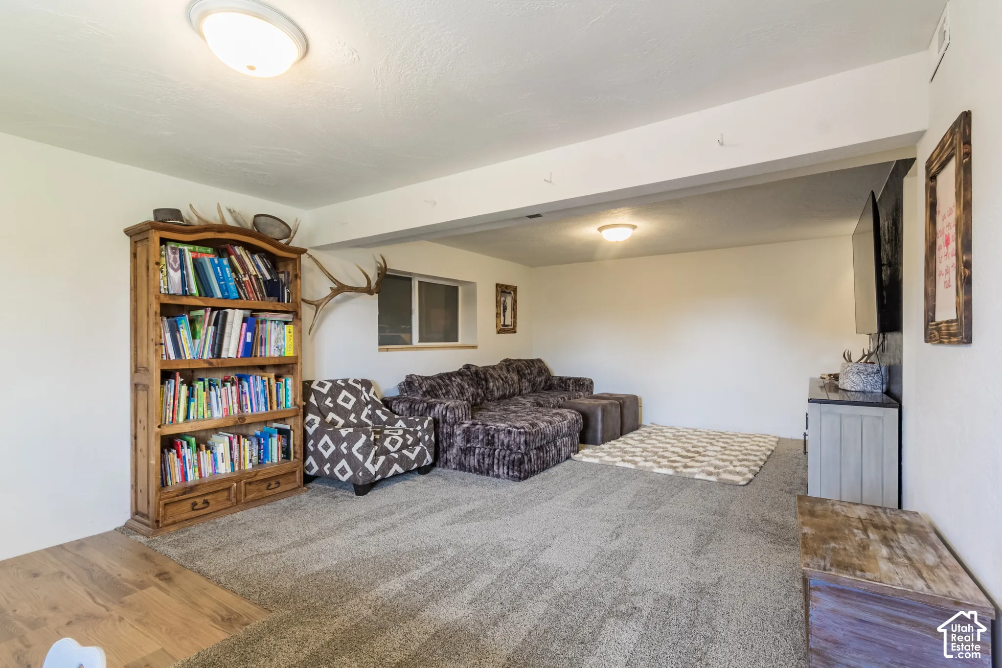 Carpeted floor, wood-finish flooring, built-in shelving unit, wall-mounted lighting, and a window for natural illumination