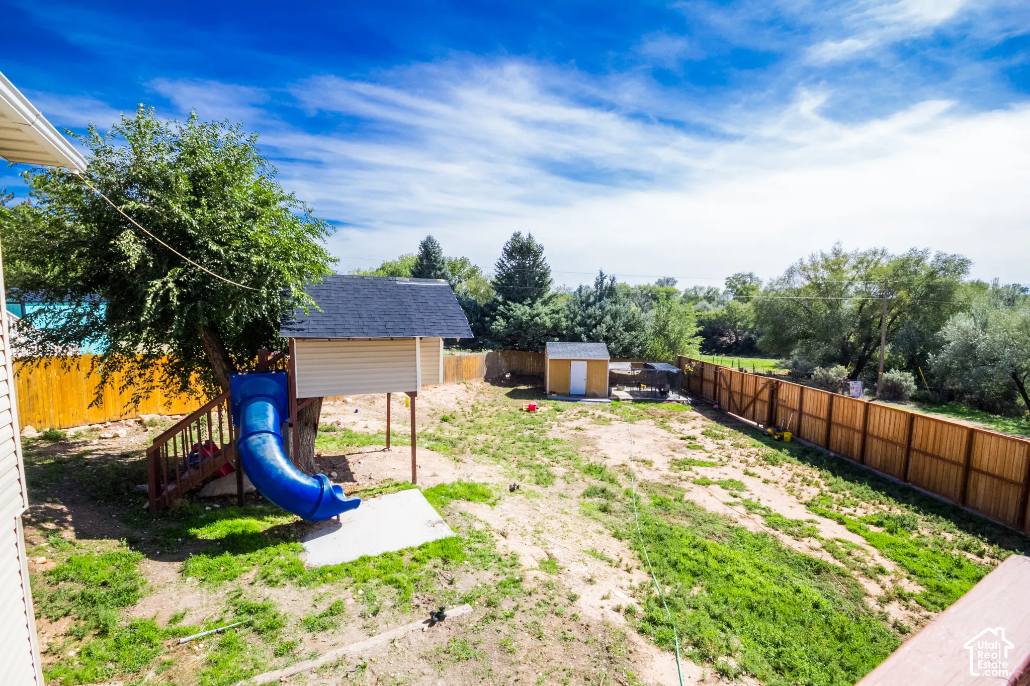 Expansive backyard with a wooden fence, mature trees, and a built-in play structure