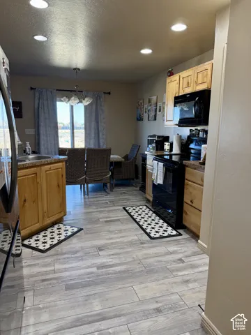 Kitchen featuring wood-finish cabinetry, black appliances, light-toned countertops, and wood-finish flooring