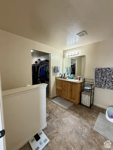Spacious room featuring wood-finish flooring, a wood-finish vanity with a built-in sink, and a wall-mounted mirror with overhead lighting