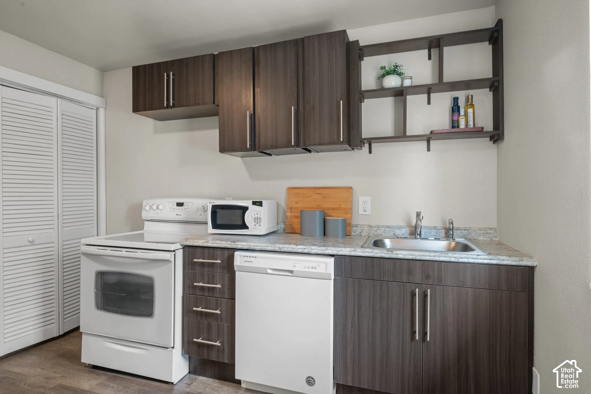 Kitchenette with wood-finish cabinetry, light-toned countertops, a stainless steel sink, and a built-in dishwasher