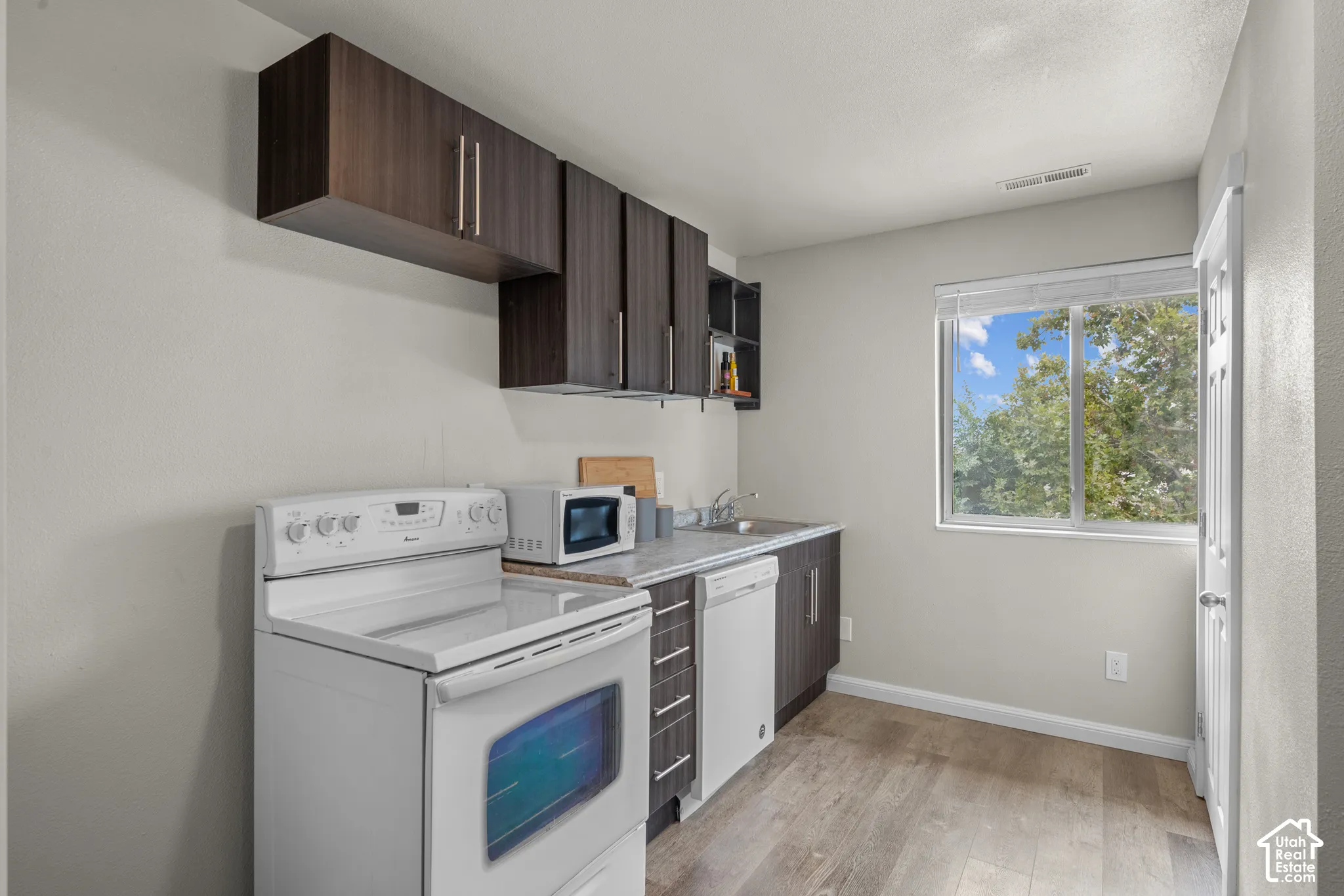 Wood-finish flooring, dark wood-finish cabinetry, and a white electric range