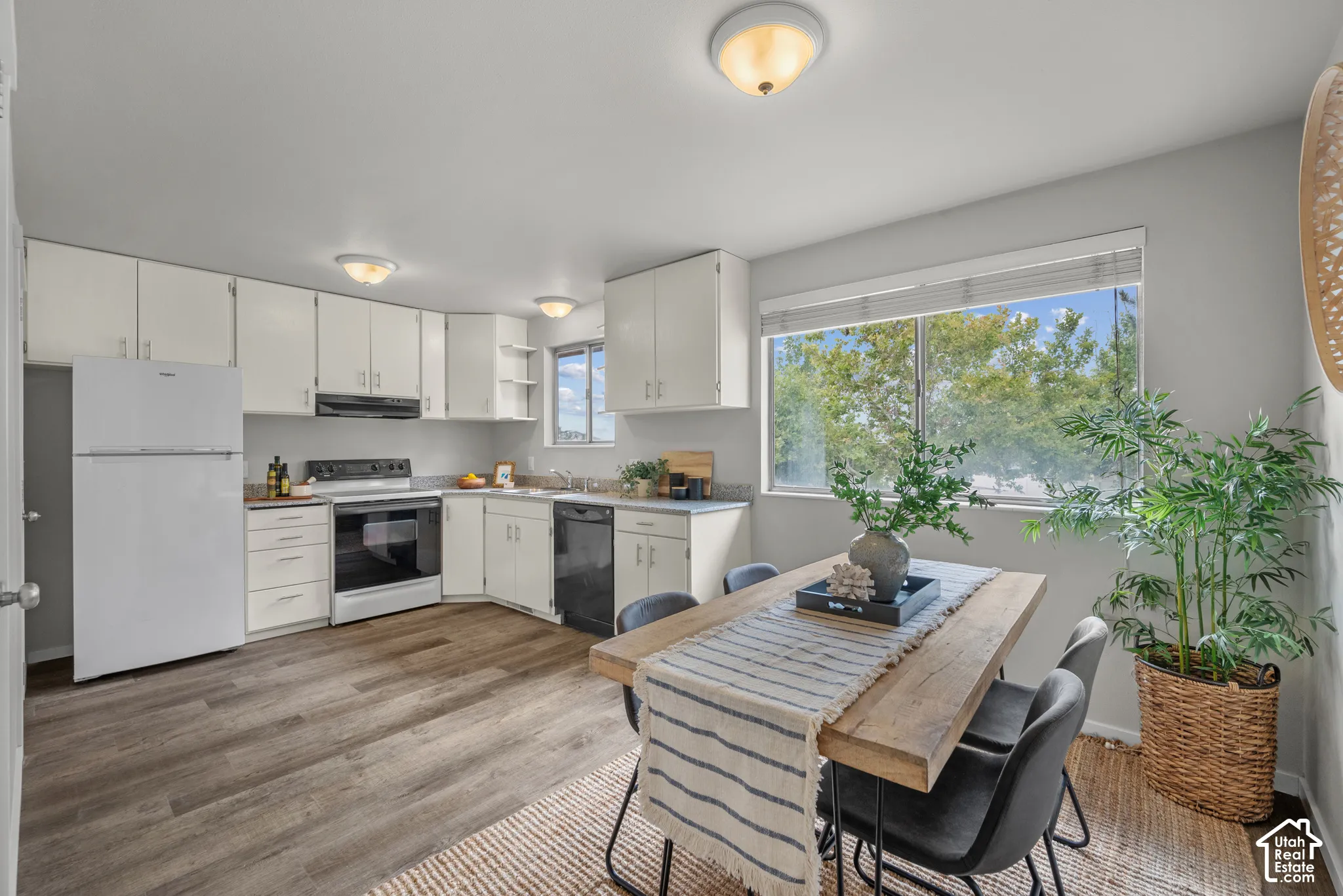 Kitchen and dining area featuring wood-finish flooring, white cabinetry, integrated appliances, and a window with outdoor scenery