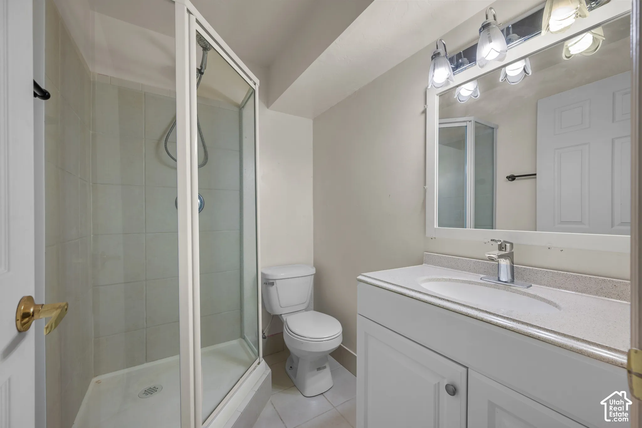 Bathroom featuring a glass-enclosed shower, white vanity with integrated sink, stone-finish countertop, and wall-mounted mirror with overhead lighting
