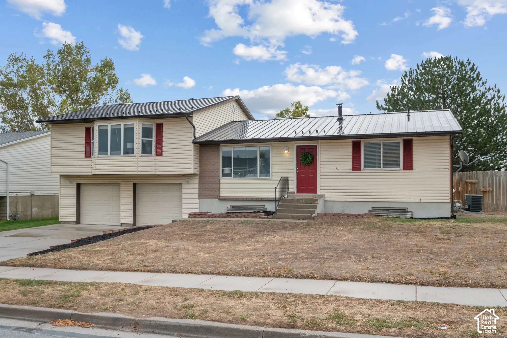 Split-level residence featuring a metal roof, light-colored siding, and red accent shutters