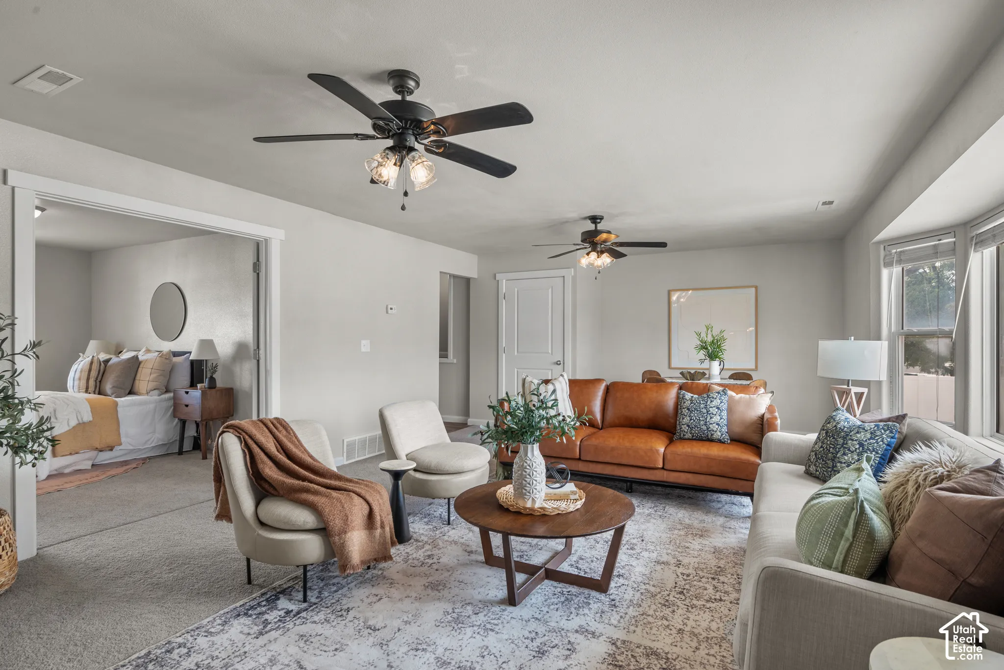 Spacious living area featuring light gray wall tones, ceiling fans with integrated lighting, wood-finish flooring, and a large bay window