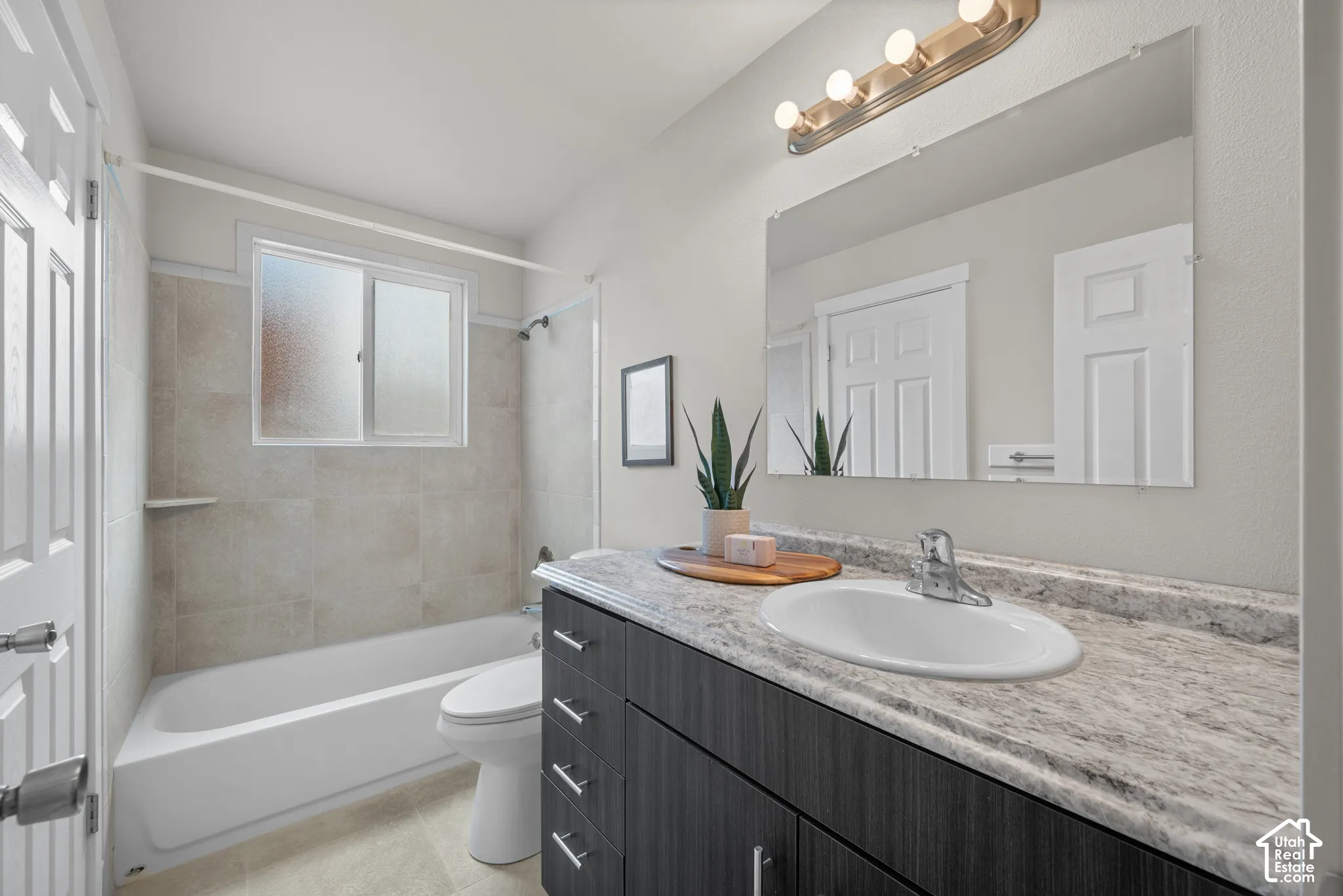 Bathroom featuring a vanity with a white countertop and undermount sink, a large wall-mounted mirror, and a full-size bathtub with tiled surround