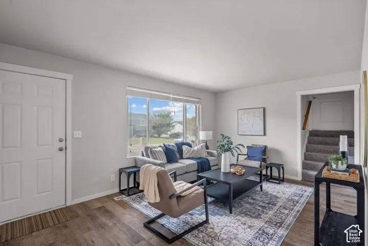 Spacious living area featuring wood-finish flooring, a large window, light-toned walls, and a carpeted staircase