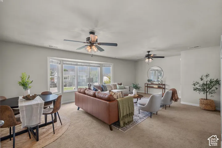 Open-concept living area with bay windows, two ceiling fans with integrated lighting, and neutral carpeting throughout