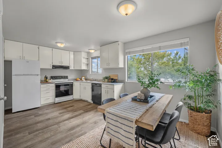 Kitchen and dining area featuring wood-finish flooring, white cabinetry, integrated appliances, and a window with outdoor scenery